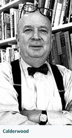 older Stan Calderwood in front of bookcases, with glasses on his head and arms folded