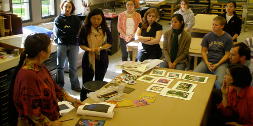 students standing around table examining small paper artwork