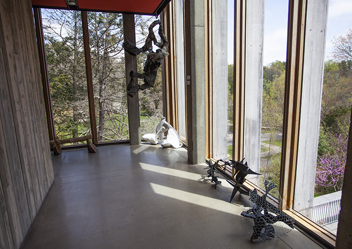 hanging and floor sculptures in a space with tall windows looking out onto trees