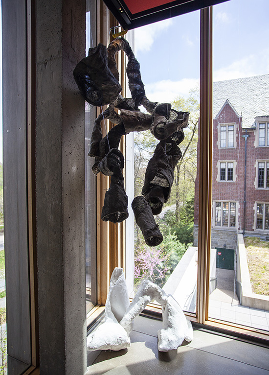 a hanging burlap sculpture installed above a white plaster sculpture on the ground in front of windows
