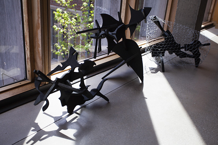 three low sculptures on the floor made of interlocking pieces of black wood; the far right sculpture has chicken wire over it
