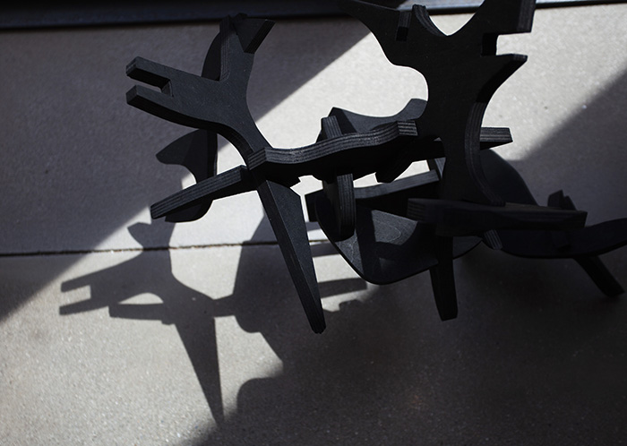 looking down at a wood sculpture made of interlocking black pieces, casting strong shadows on the floor