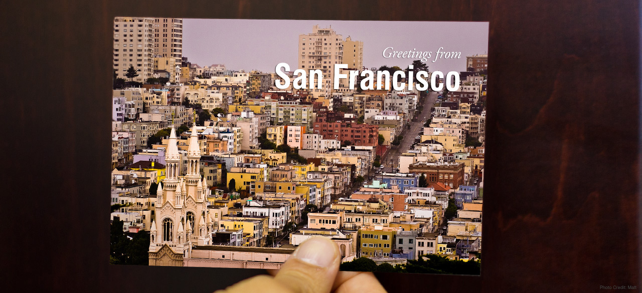 Hand holds a postcard that reads "greetings from San Francisco"
