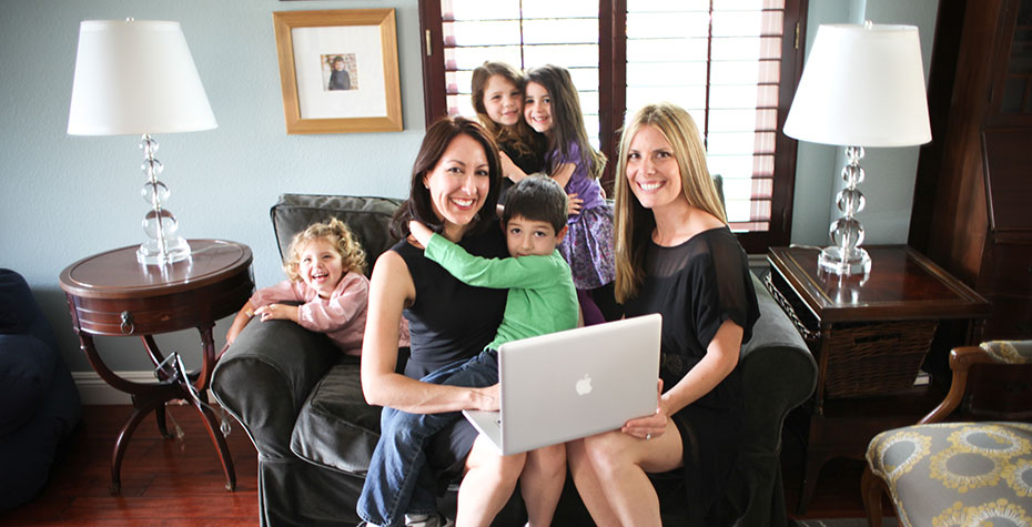 Erin Giglia, Laurie Rowen, and their respective children pose with a laptop on a couch