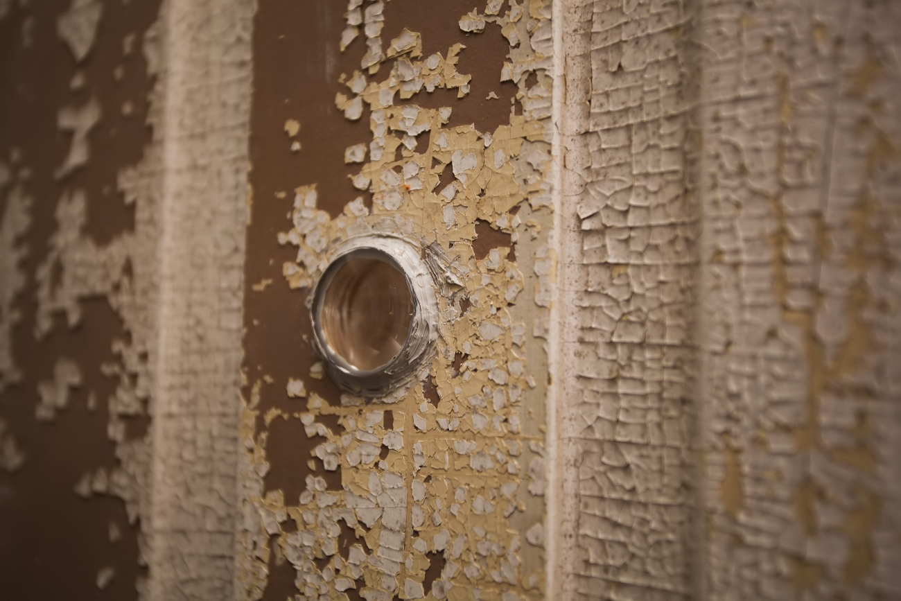 closeup of peephole in brown door with peeling tan paint