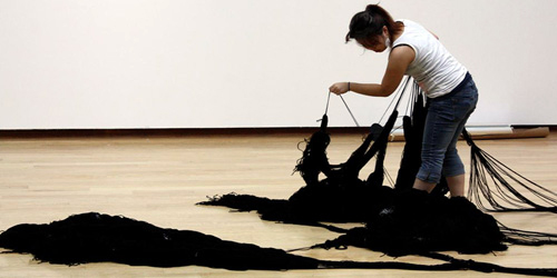 student handling artwork consisting of mass of black strings