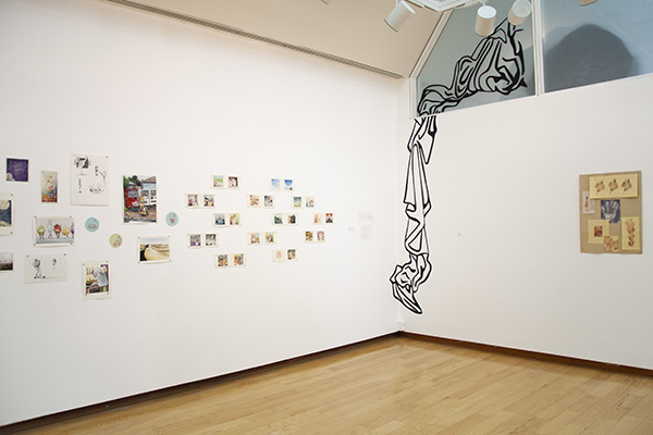 gallery view showing black vinyl line art piece installed in the corner, with many small drawings on left wall and single collage print on right wall