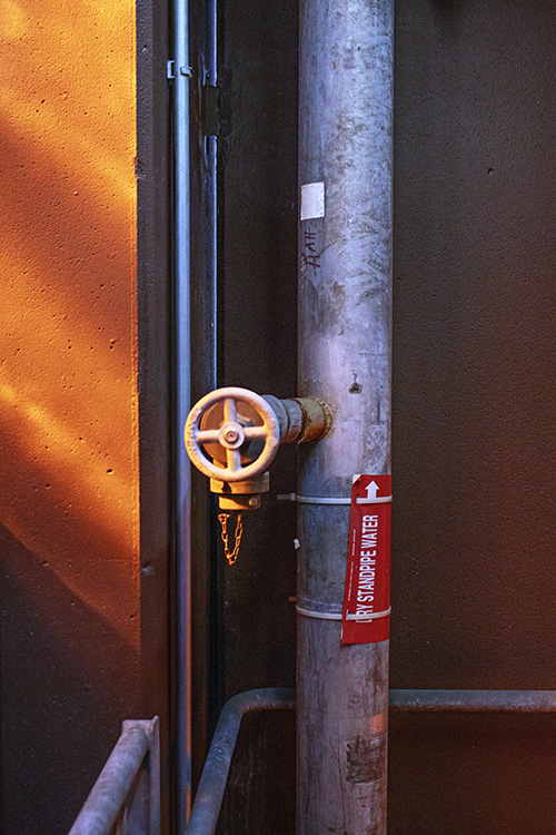large vertical pipe with a wheel on it, dramatically lit by raking orange-yellow light