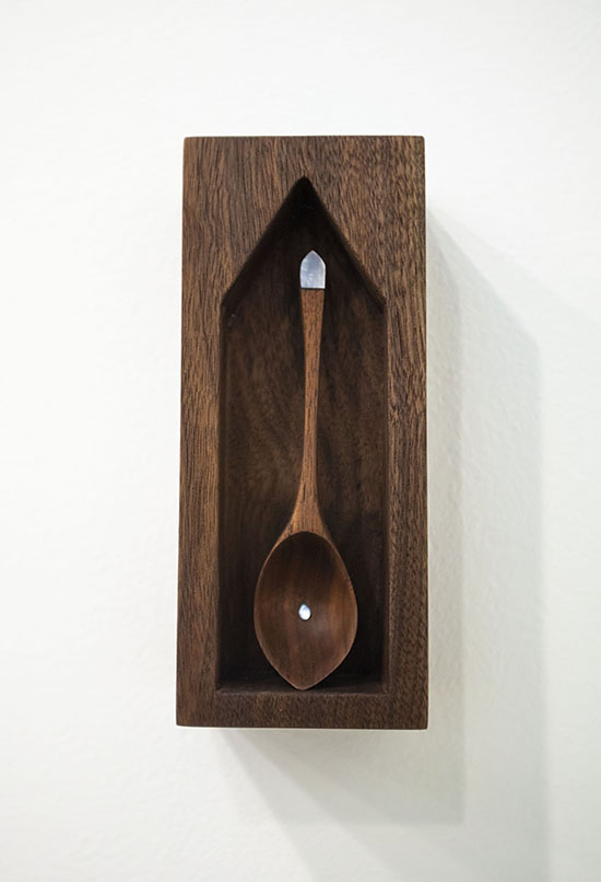 dark wood box mounted on the wall with house-shaped cavity, slender wood spoon with mother of pearl accents resting vertically inside