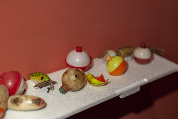 photo of discarded colorful plastic fishing floats laid out on a white styrofoam shelf against a red-orange wall