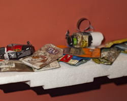 photo of various pieces of trash laid out on a white styrofoam shelf against a red-orange wall