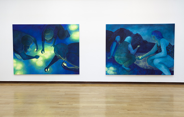 two large predominantly blue paintings of women performing mysterious actions with yellow glowing orbs, installed on a white gallery wall