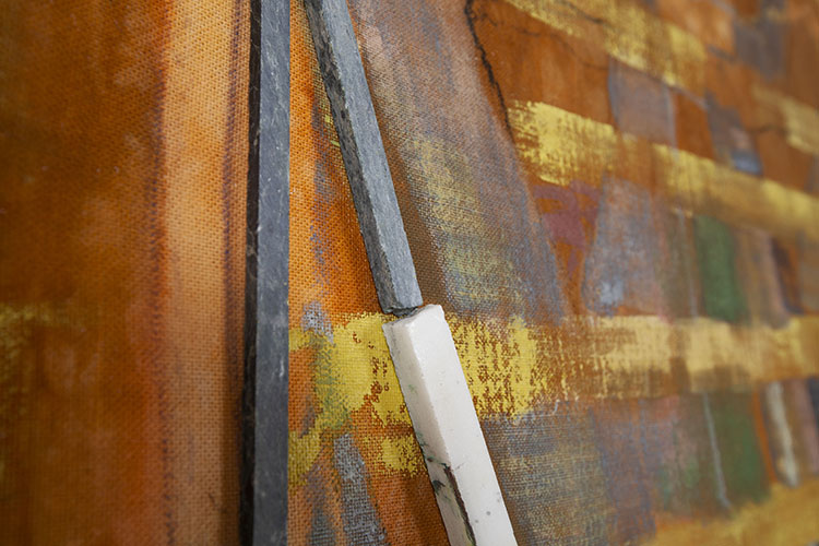 detail of a predominately orange and yellow painting with gray and white stone rods attached to the surface