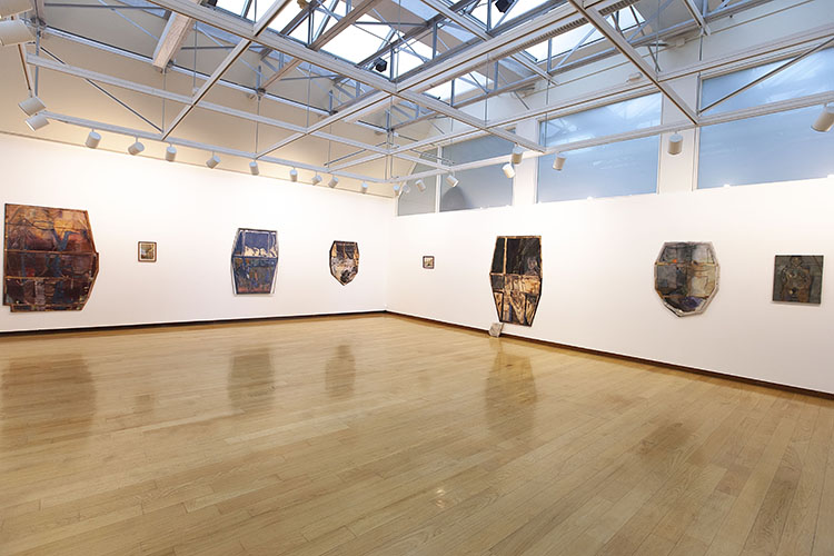 white walled, wood floored gallery with large, irregularly shaped abstract paintings on the walls