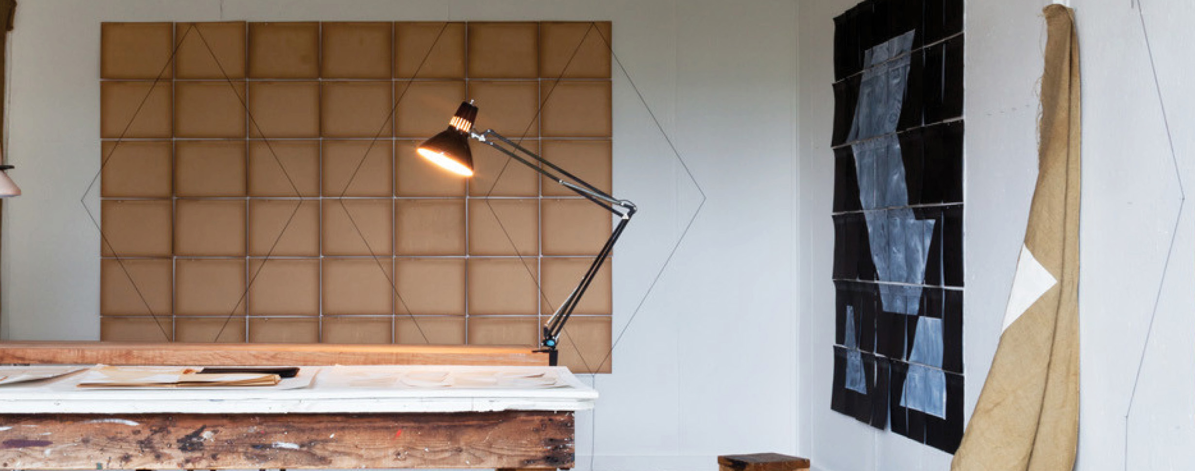 studio work table with clamped light; tan grid behind with thin lined diamond shapes laid on top
