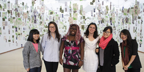 group of students standing in front of hanging postcard-sized work