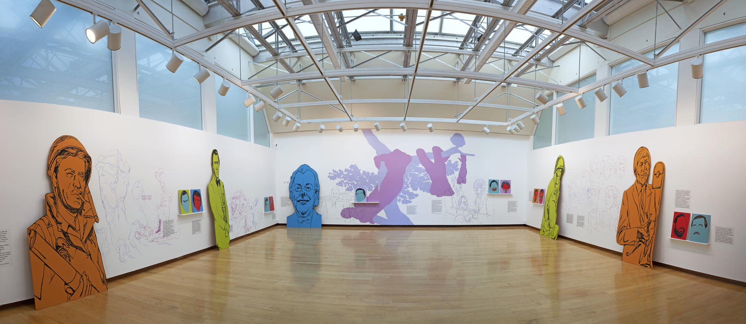wide view of the gallery with large colorful figurative cut-outs and other artwork against the walls