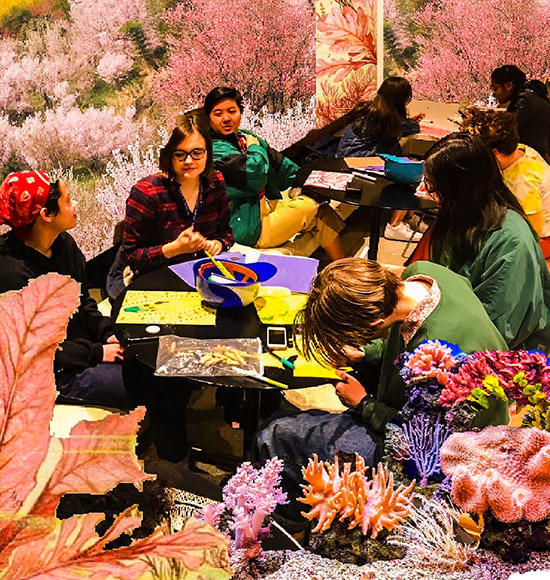 students gathered at art-making event with flowers collaged around the edges of the image