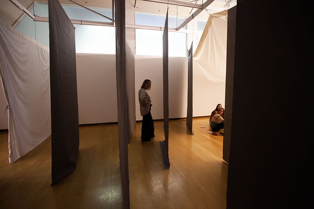 side view of dark staggered hanging panels of fabric, with a person standing between them