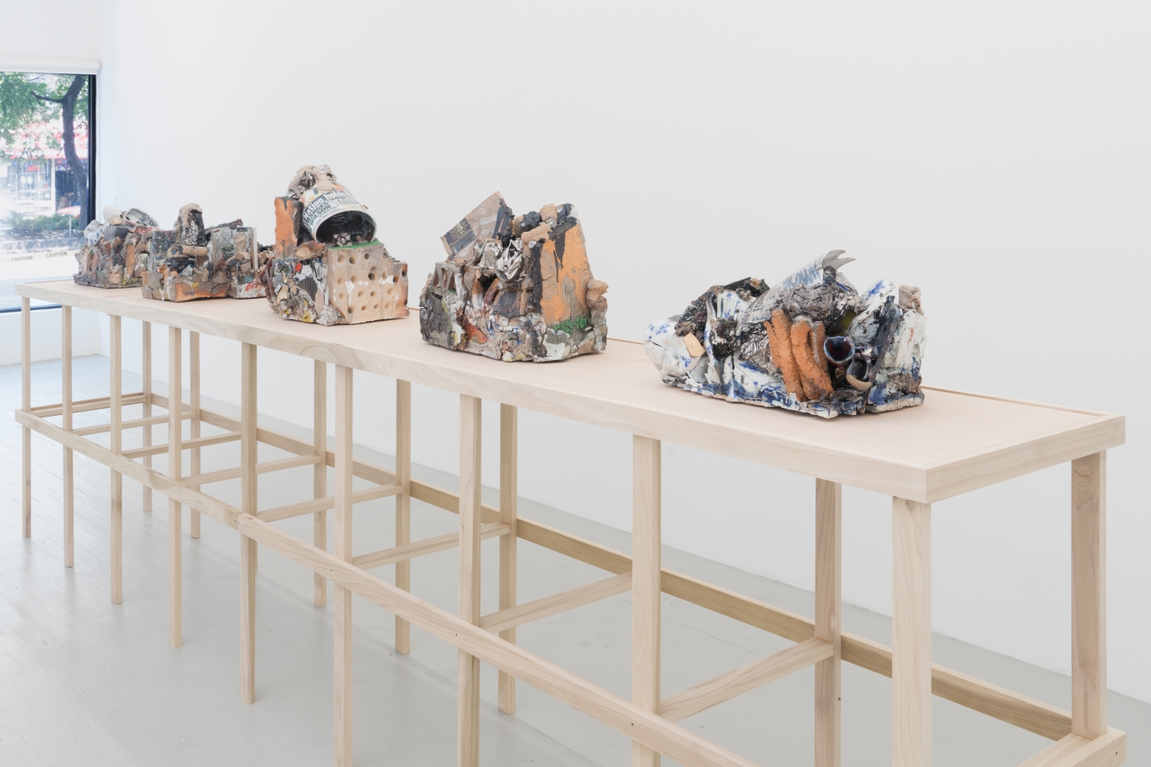 ceramic sculptures on light wood table in white gallery space