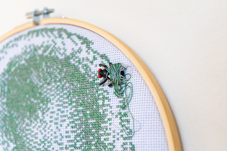 close up of plastic fly attached to embroidery with green and silver thread