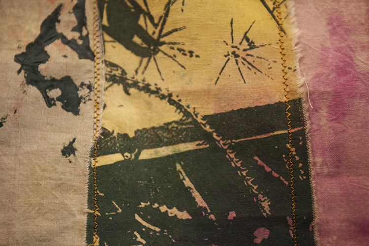 close up on a textile piece with fabric printed in abstract and botanical forms in ink shades of pink, yellow, and green; a golden yellow zigzag stitch connects pieces of fabric