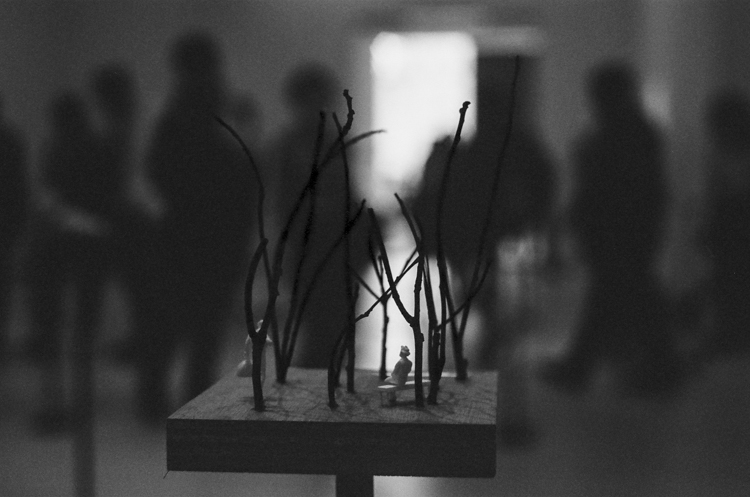 black and white photo of sculpture on stand in foreground with blurry patrons in background