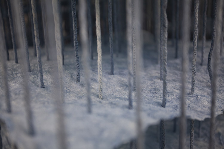 close up on a section of a large paper and cotton cord installation, showing a handmade sheet of indigo-dyed paper, pierced through with many vertical, dyed cords