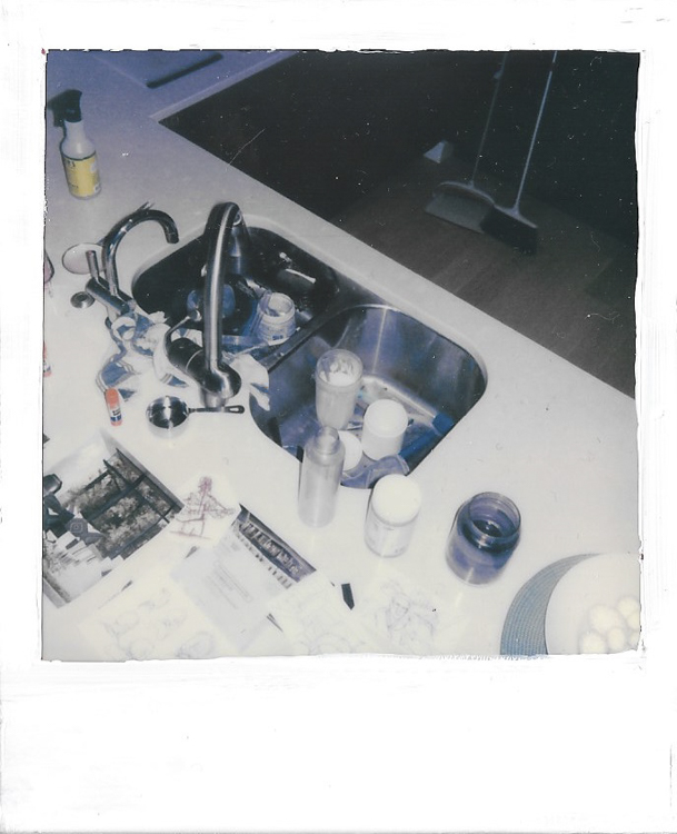 polaroid of double sinks with many items in and around them, shot from high angle