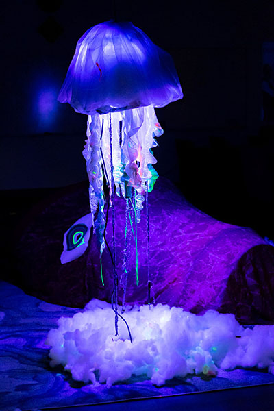 hanging fabric jellyfish lit from within by intense blue light, soft materials below