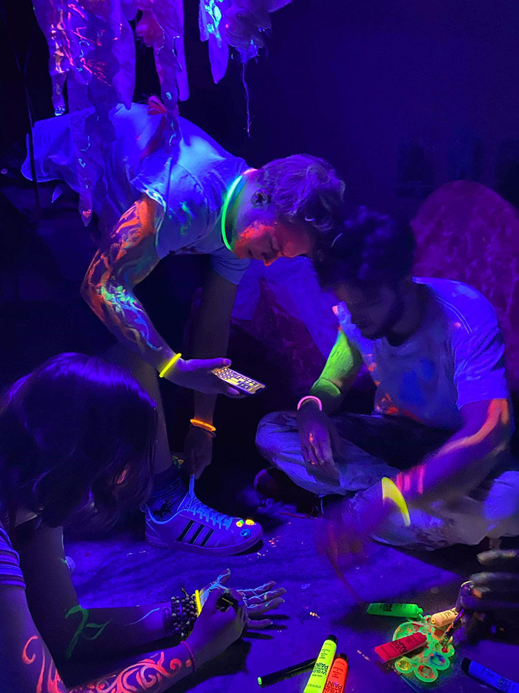 figures in dark space painting on themselves with neon paint that glows in black light
