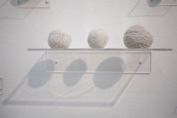 three balls of white yarn on a clear shelf with shadows below
