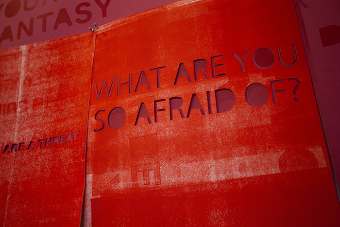 close-up of overlapping bright red prints. The closest has cut-out text reading 'WHAT ARE YOU SO AFRAID OF?'