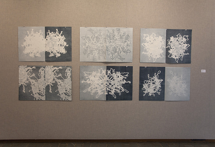 six large double prints in blue and white on a grayish fabric wall, showing yarn and tangle imagery